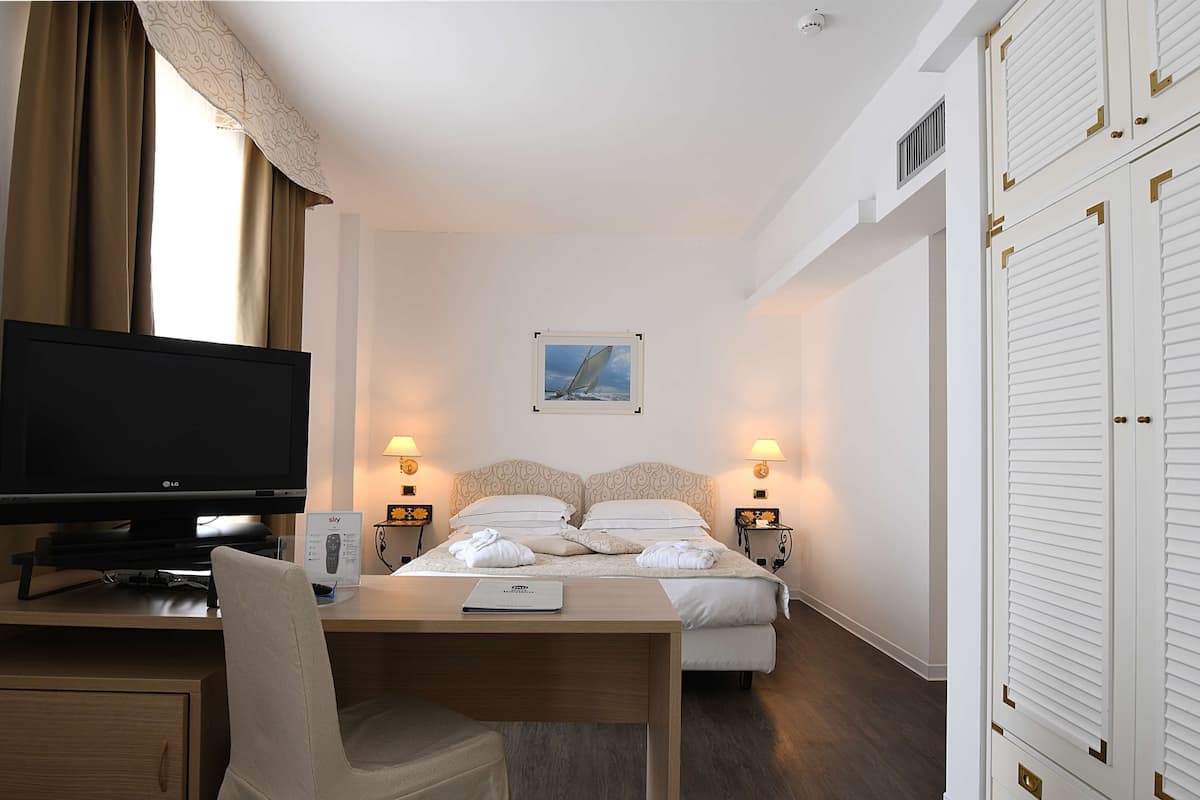 Une chambre d’hôtel avec un lit, un bureau avec une télévision et une chaise.