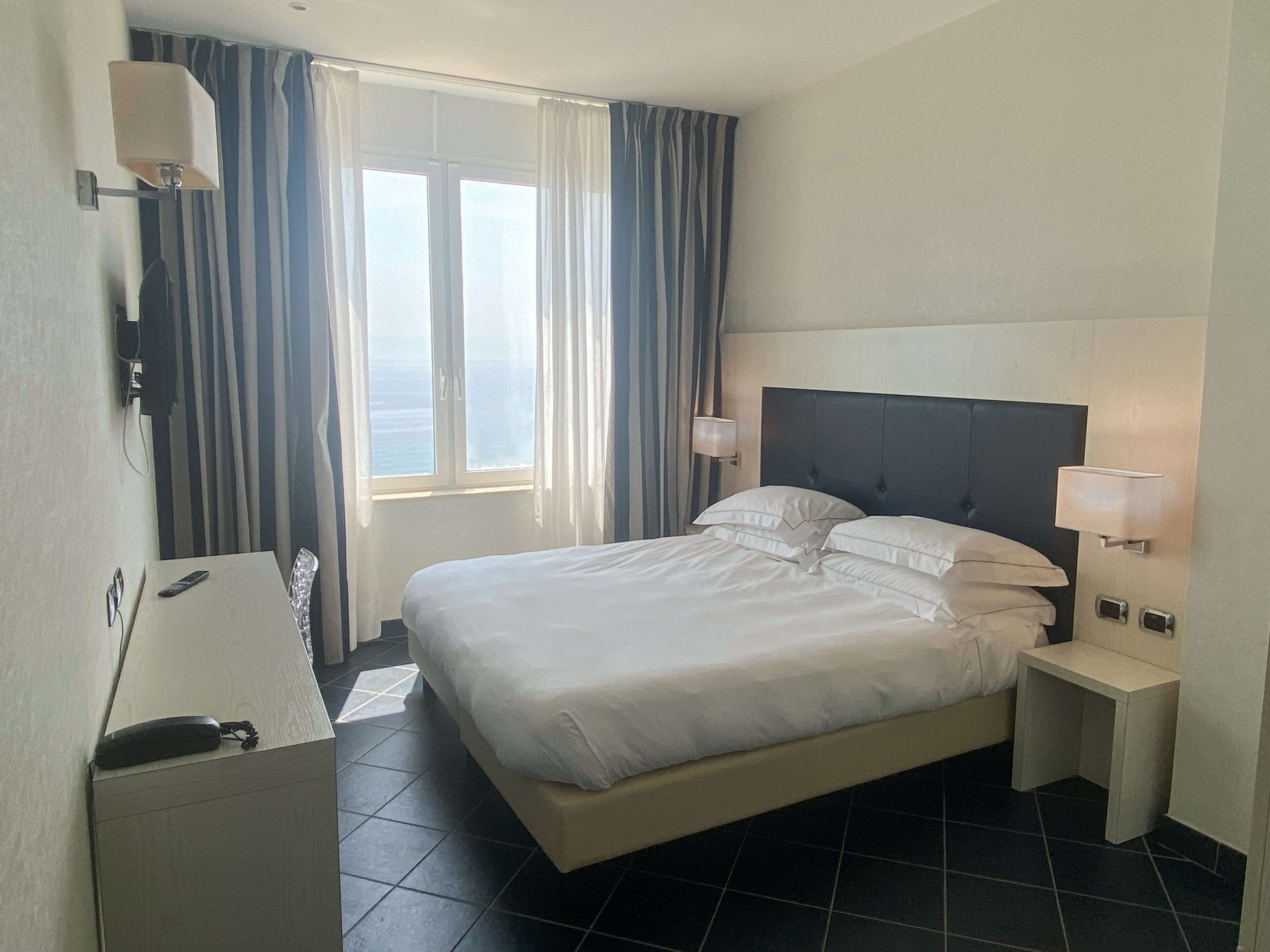 A hotel room with a bed, bedside tables, a lamp, a phone, and a window with curtains.