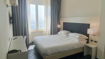 A hotel room with a bed, bedside tables, a lamp, a phone, and a window with curtains.