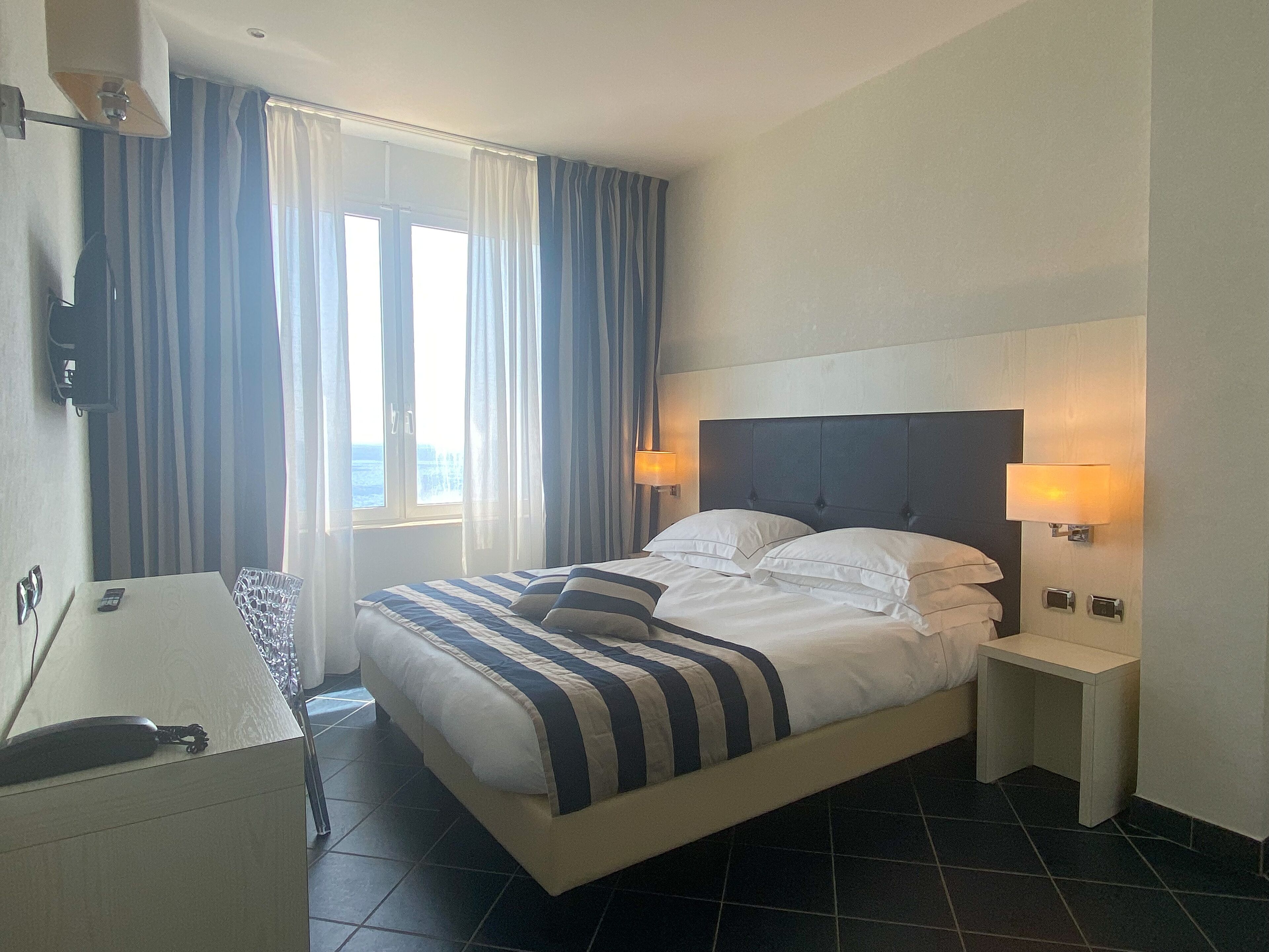 A hotel room with a bed, bedside lamps, a desk, and a window with curtains.