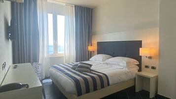 Una habitación de hotel con una cama, lámparas de noche, un escritorio y una ventana con cortinas.