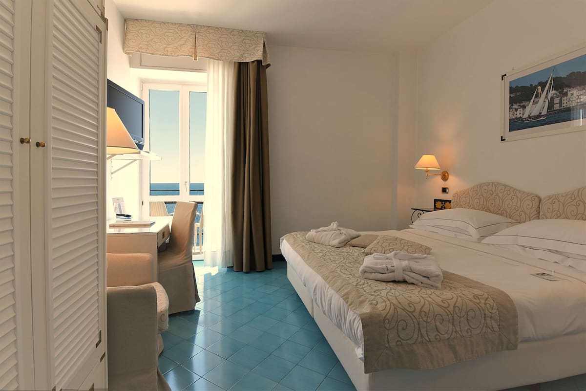Une chambre d’hôtel avec un lit, un bureau, une chaise, une télévision et une fenêtre avec des rideaux.