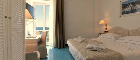 A hotel room with a bed, a desk, a chair, a TV, and a window with curtains.