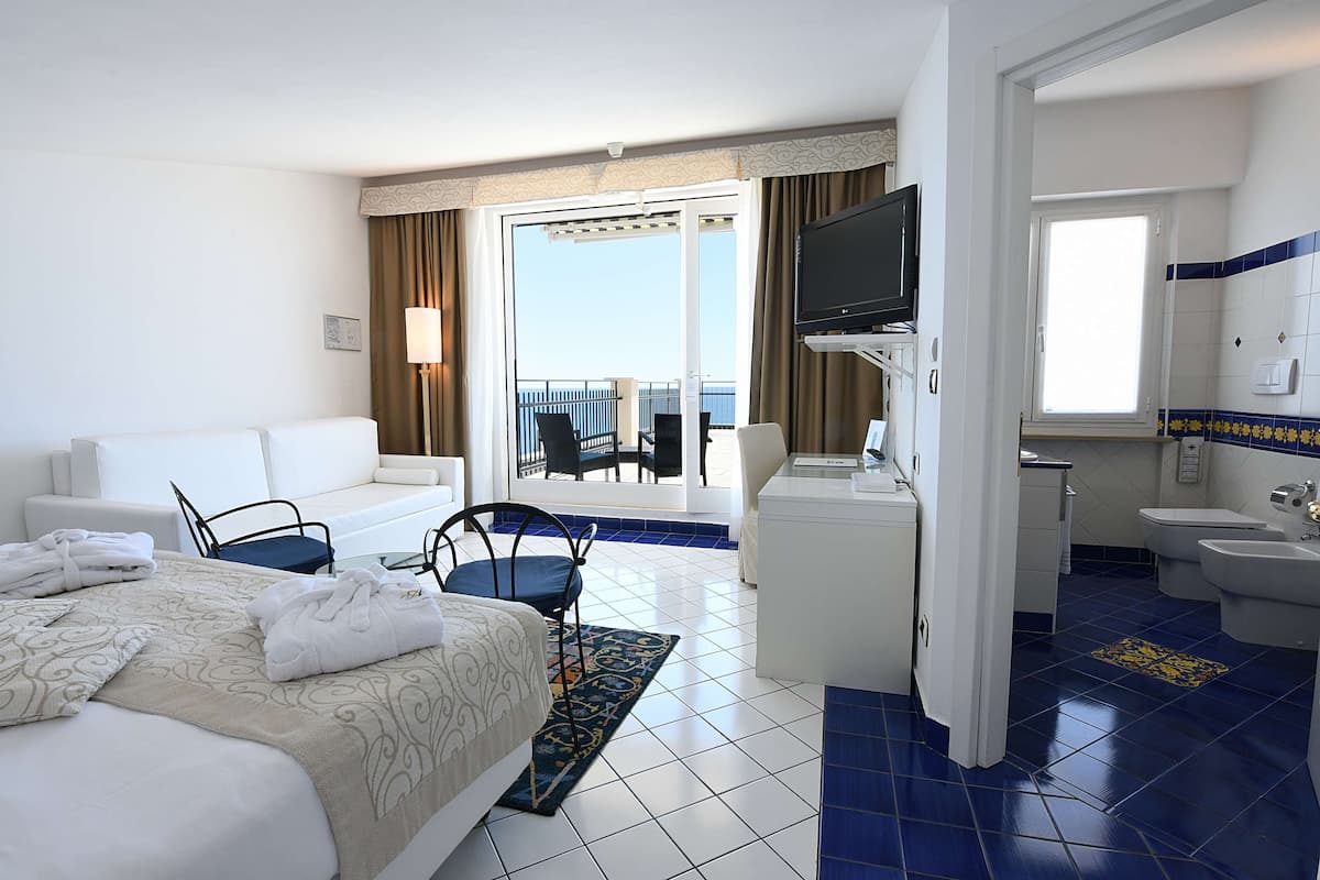 Une chambre d’hôtel comprenant un lit, un canapé, une télévision, un balcon avec vue et une salle de bain avec un lavabo et des toilettes.