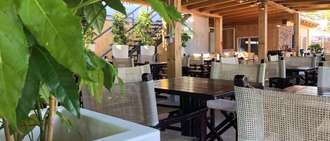 An outdoor seating area with tables and wicker chairs, surrounded by potted plants.