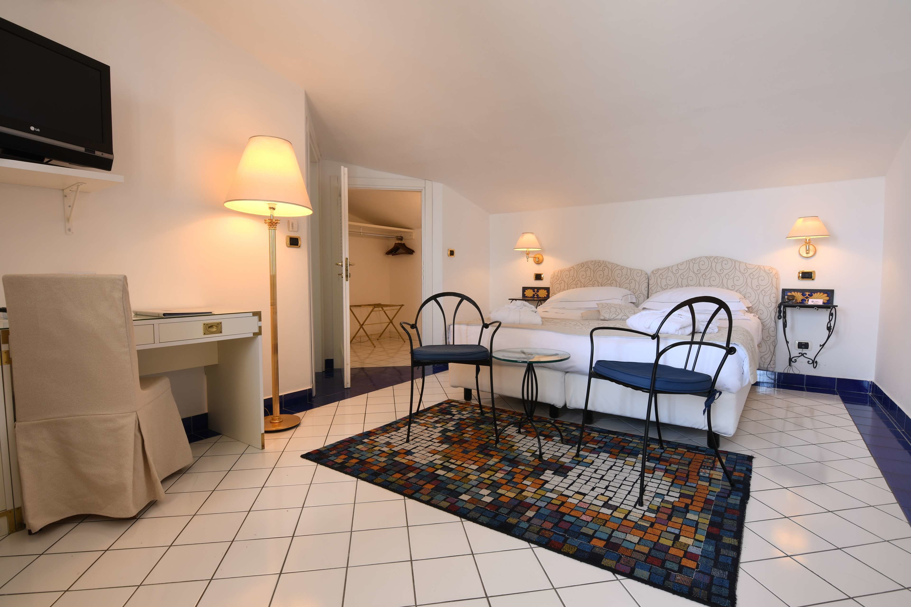 Een hotelkamer met een bed, nachtkastjes, een bureau, een stoel, een televisie en een kamerbreed tapijt met een patroon.