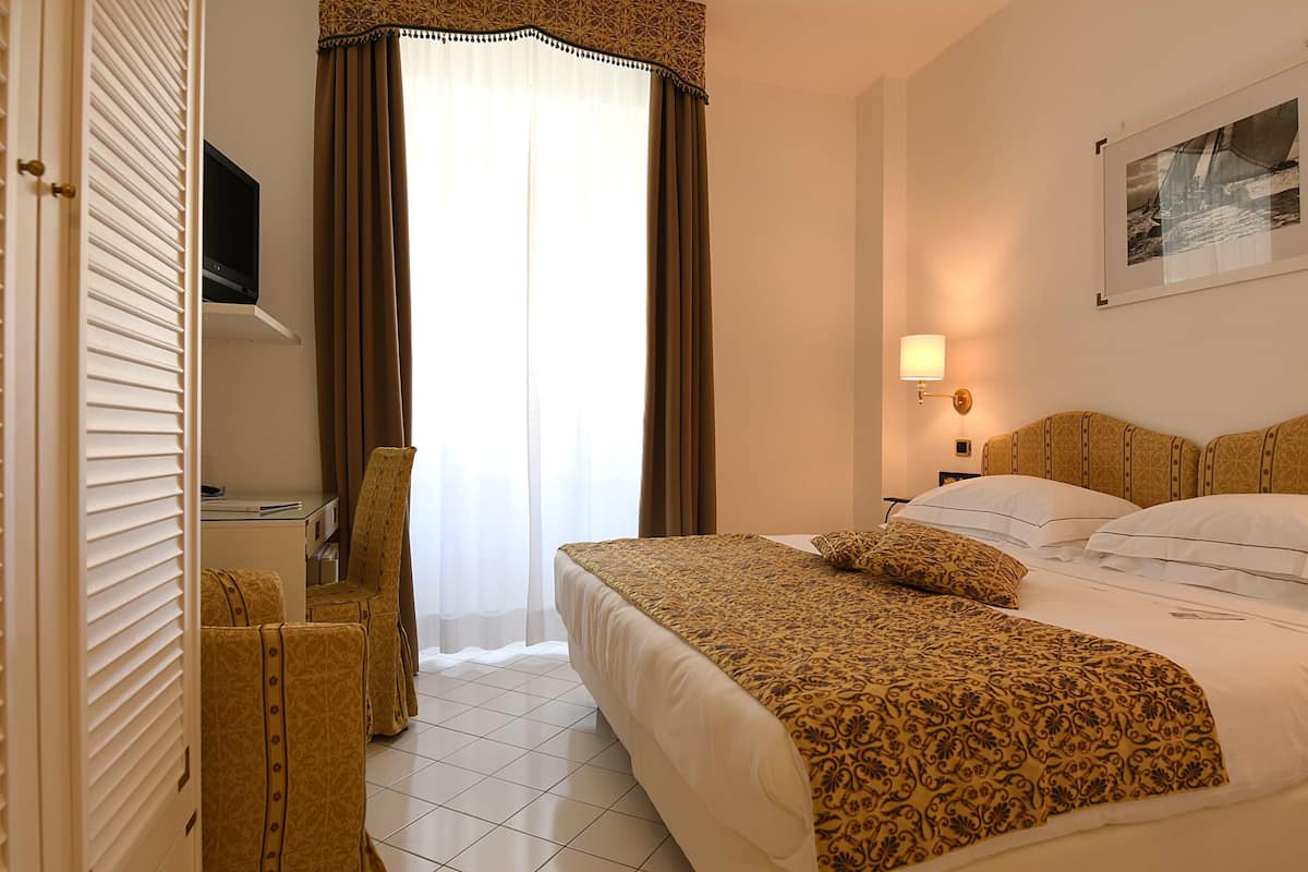 Une chambre d’hôtel équipée d’un lit, d’un bureau, d’une chaise, d’une télévision et d’une fenêtre avec des rideaux.