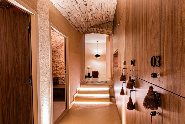 A hallway with a stone wall, wooden door, and steps leading to a room with a hanging lamp and a small table. - Cèdre Beaune, A Beauvallon Hotel & Spa (Beaune)