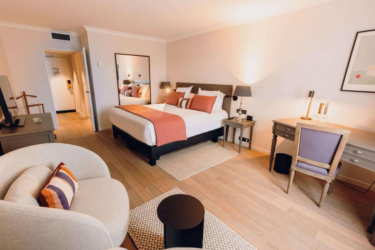 A hotel room with a bed, a desk, a chair, a sofa, and a small table.