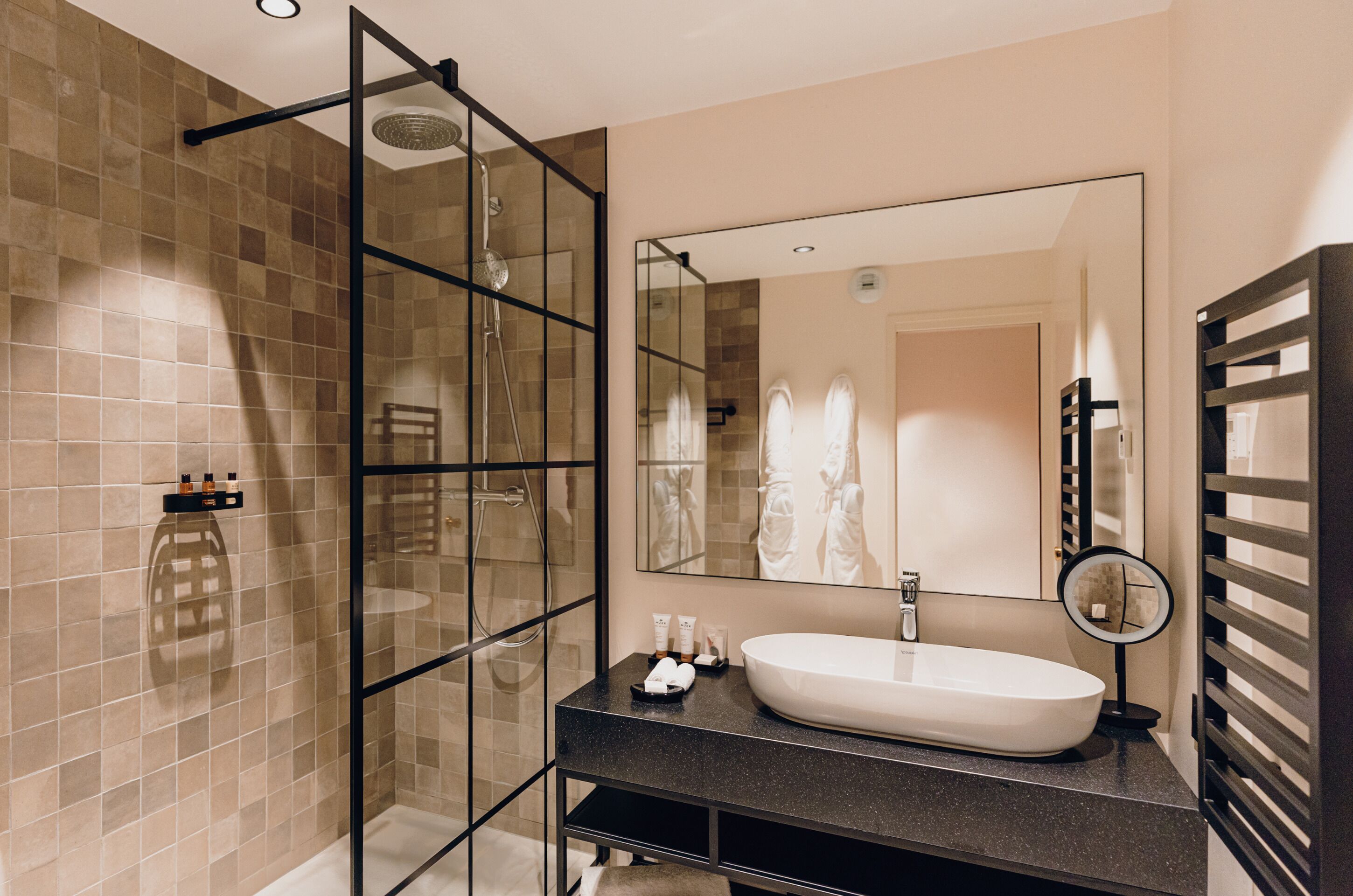 Une salle de bain moderne avec une douche à parois de verre, un grand miroir et un plan de toilette noir avec un lavabo blanc.