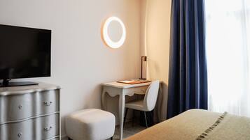 A hotel room with a desk, chair, television, and a bedside table.