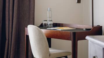 A hotel room with a wooden desk, a chair, a lamp, a bottle, and a book.