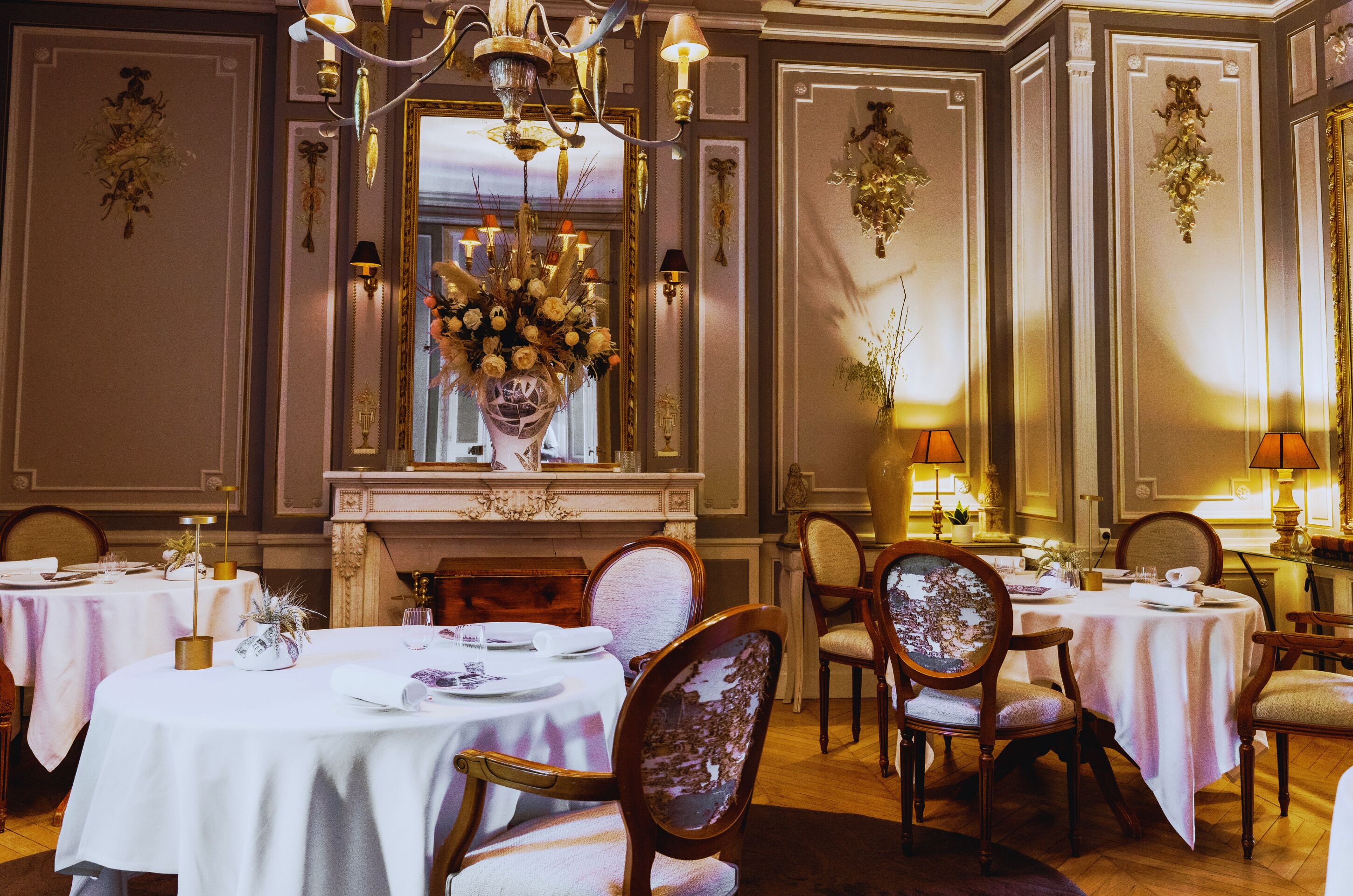 A dining area with round tables, chairs, and a chandelier.
