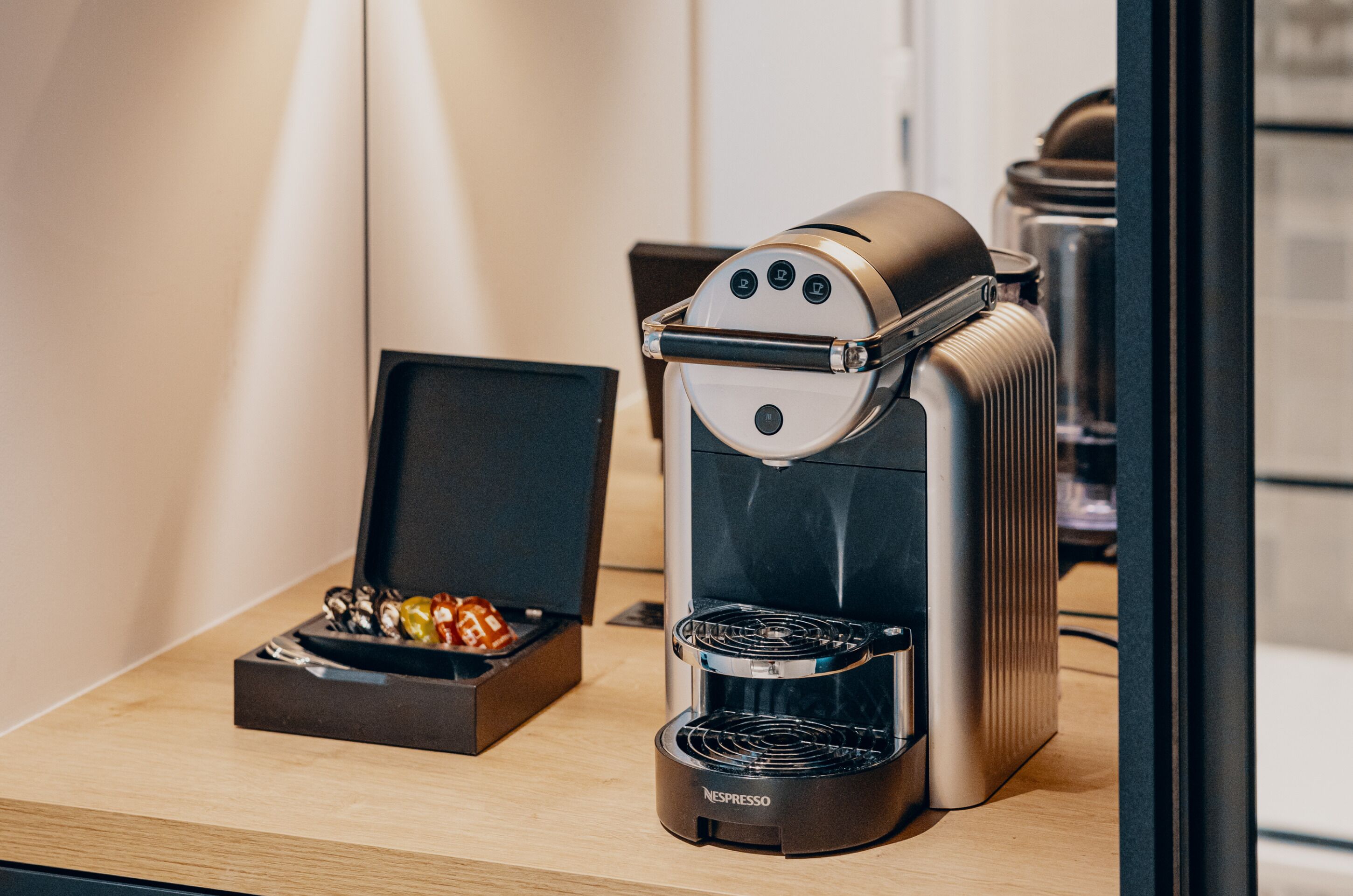 A Nespresso coffee machine on a wooden surface with a box of coffee capsules beside it.