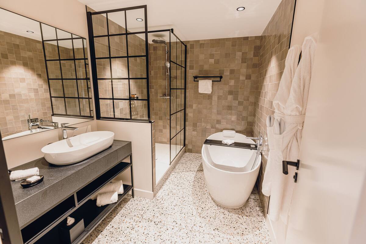 A modern bathroom with a large mirror, two sinks, a walk-in shower, and a bathtub.