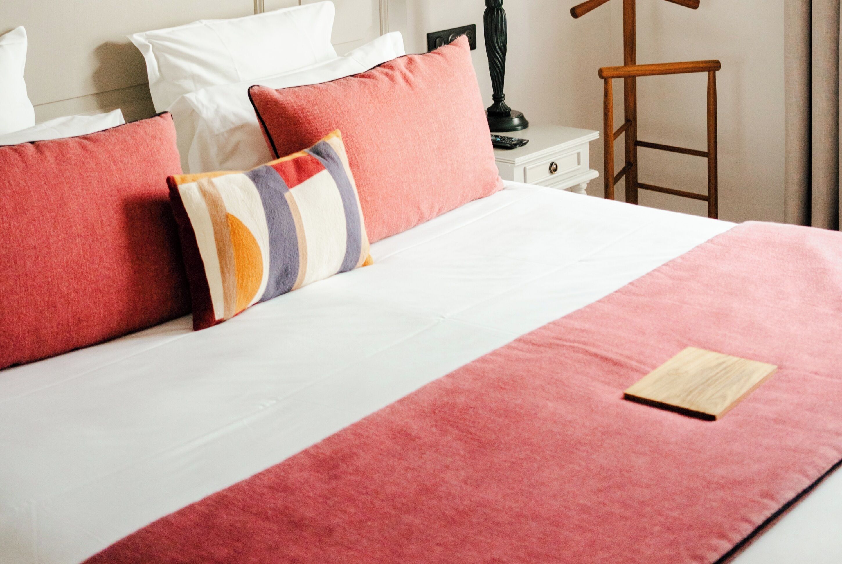 A neatly made bed with a white and red bedspread, multiple pillows, and a wooden tray on the bed.