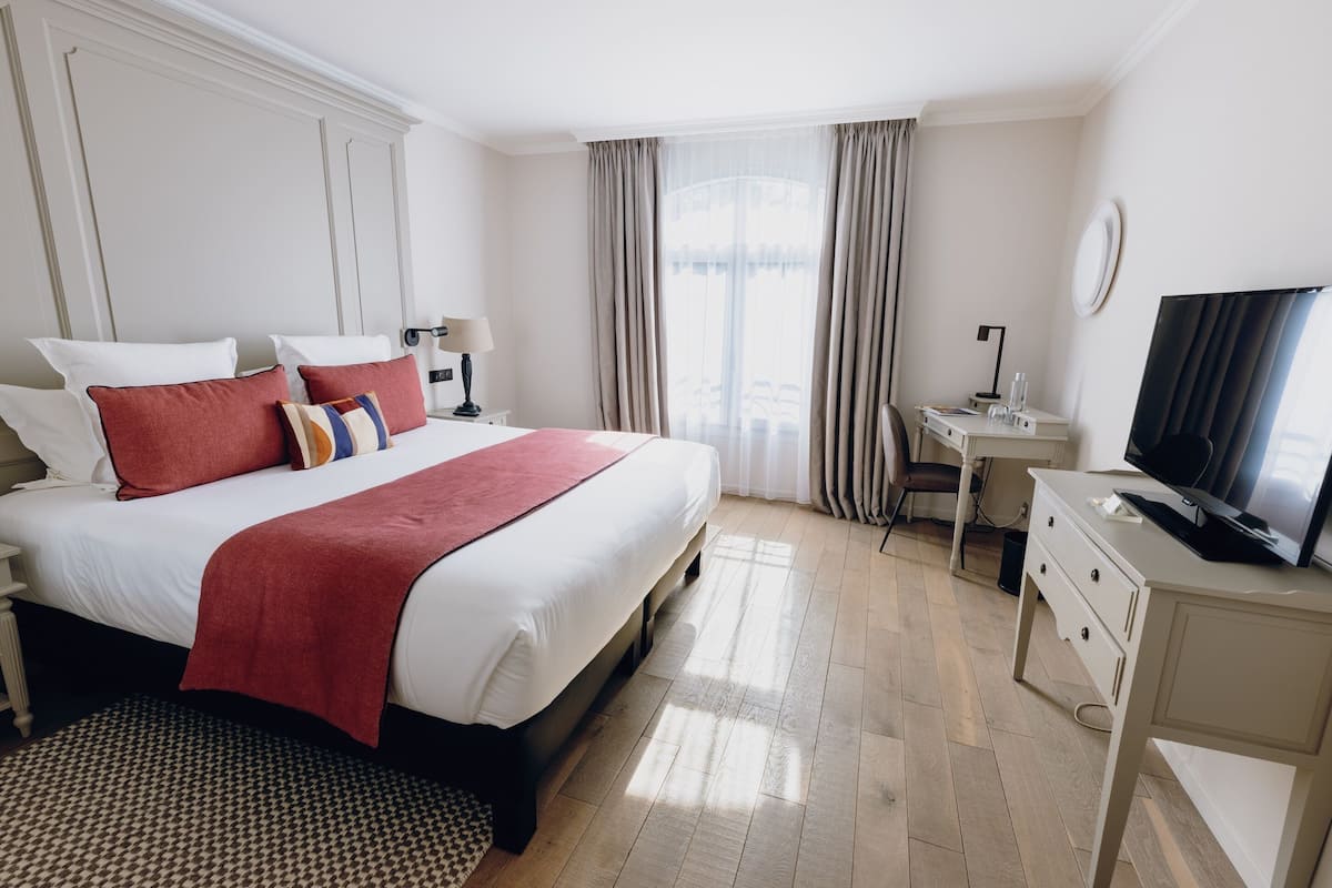 A hotel room with a large bed, a desk, a television, and a view of the city.