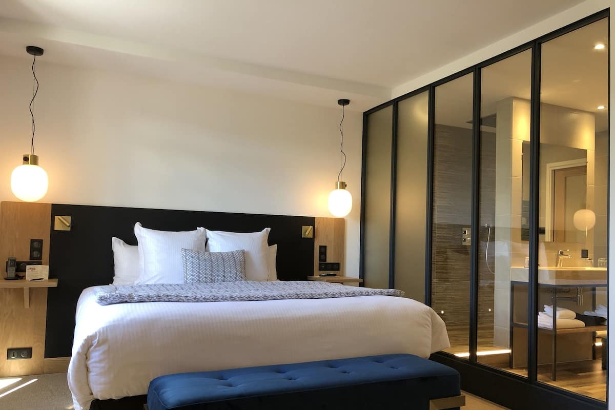 A modern hotel room with a large bed, bedside tables, a bench, and a large mirror.