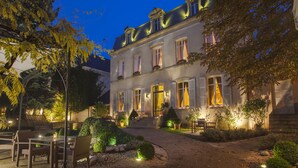A two-story building with a well-lit entrance, a paved driveway, and outdoor seating. - Cèdre Beaune, A Beauvallon Hotel & Spa (Beaune)