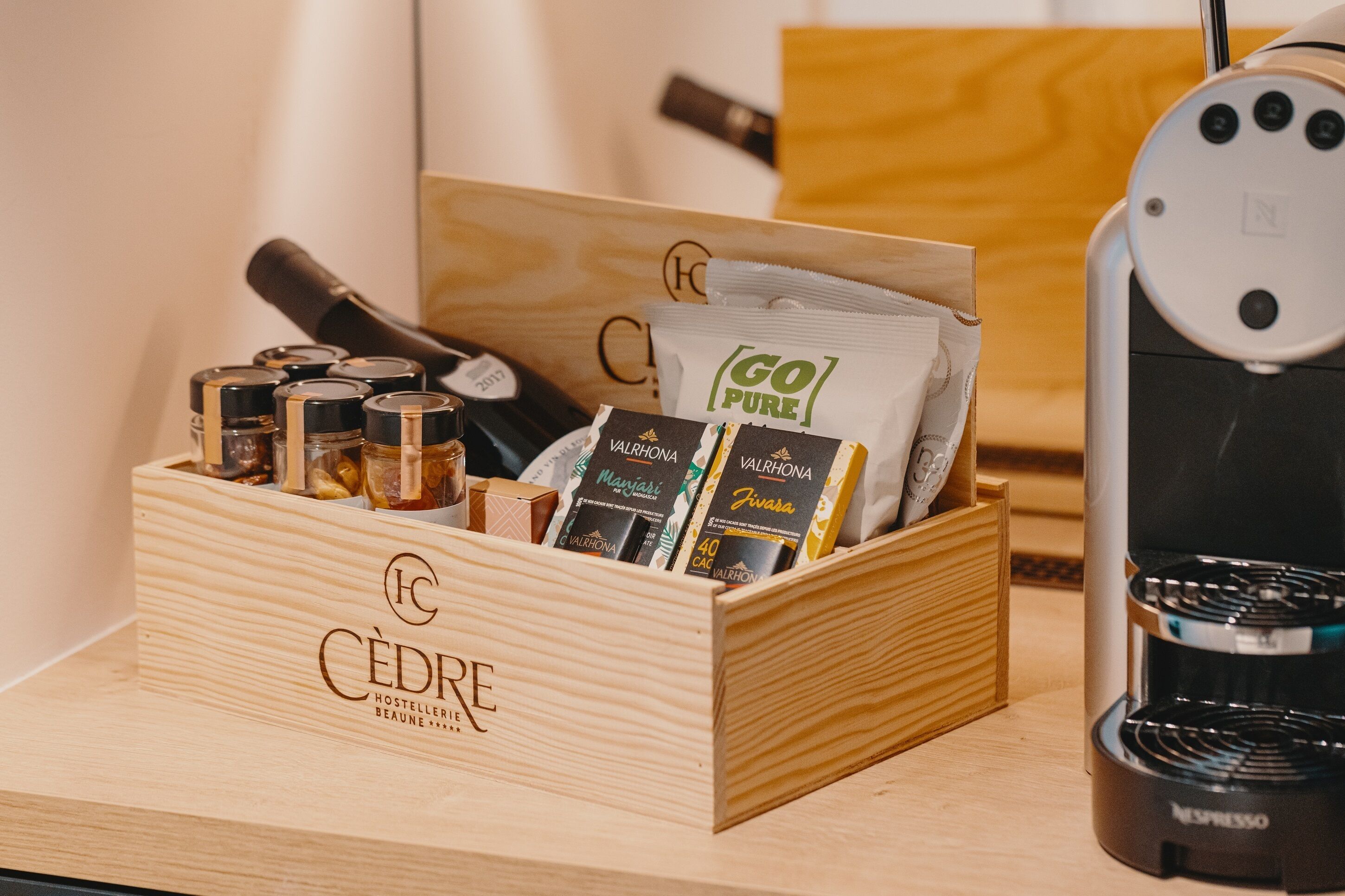 Una caja de madera con la etiqueta 'CÉDRE HOSTELLERIE BEAUNE' que contiene granos de café y un molinillo.