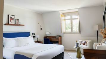 Une chambre d’hôtel avec un lit, un bureau, une chaise, une petite table avec une lampe et une fenêtre.