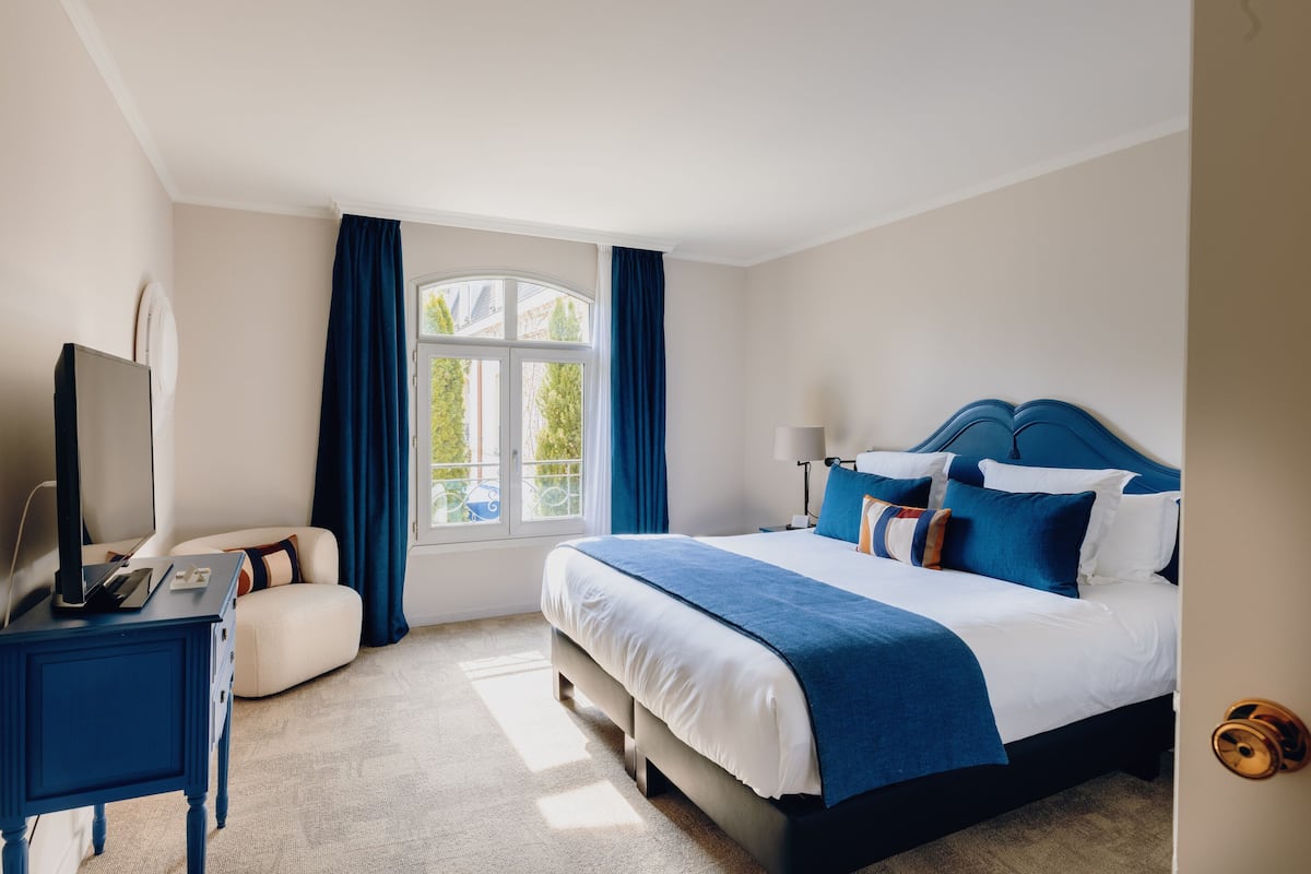 A hotel room with a bed, a desk, a chair, a TV, and a window with curtains.