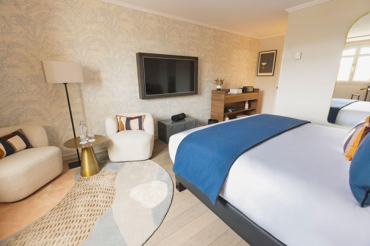 A hotel room with a bed, a sofa, a chair, a TV, a wooden cabinet, and a mirror.