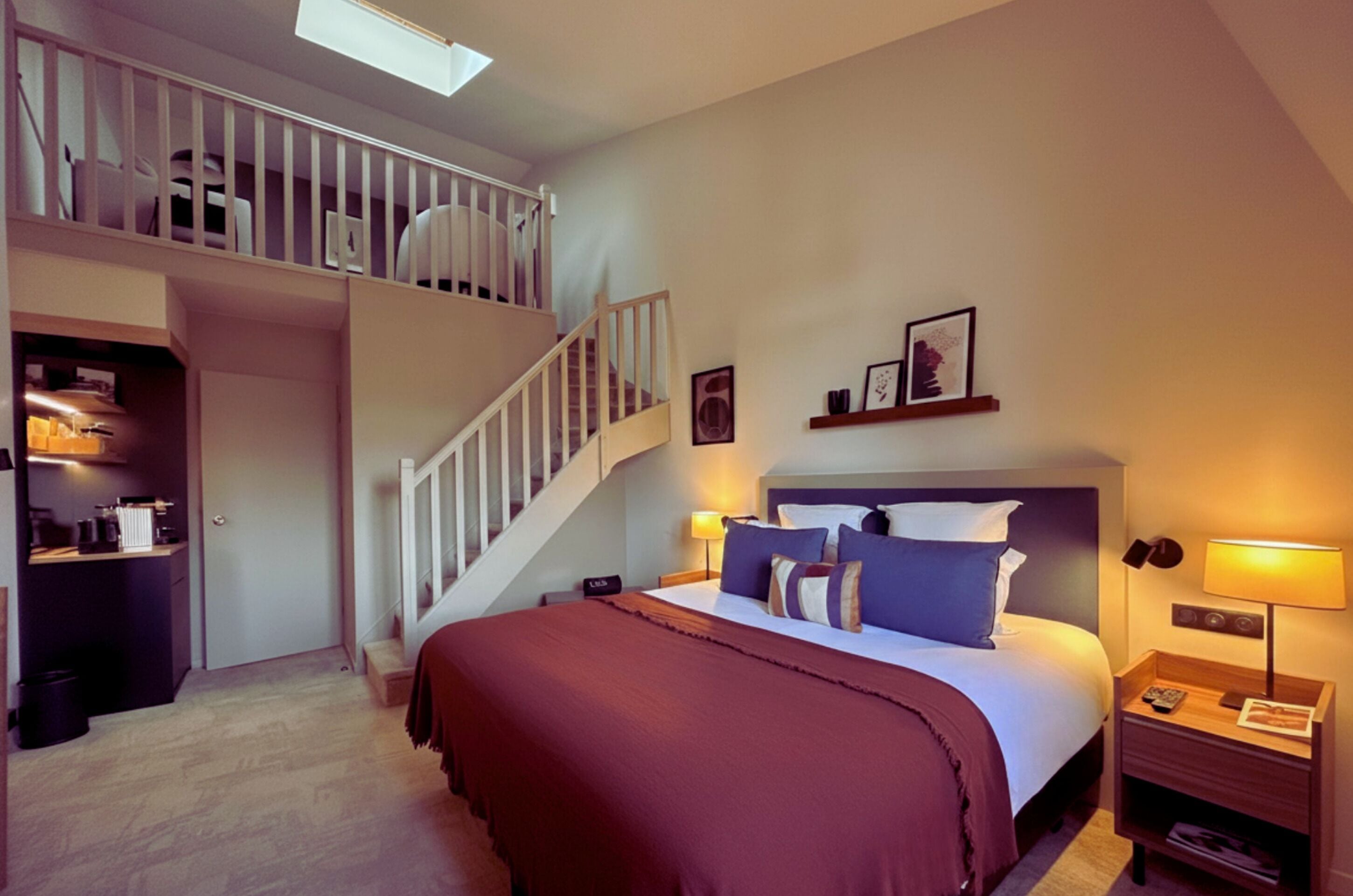 A bedroom with a bed, a nightstand, a lamp, a staircase, and a shelf with pictures.