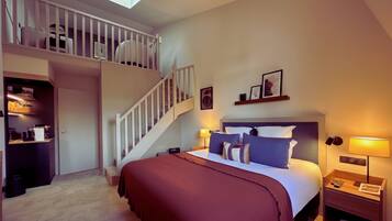 A bedroom with a bed, a nightstand, a lamp, a staircase, and a shelf with pictures.
