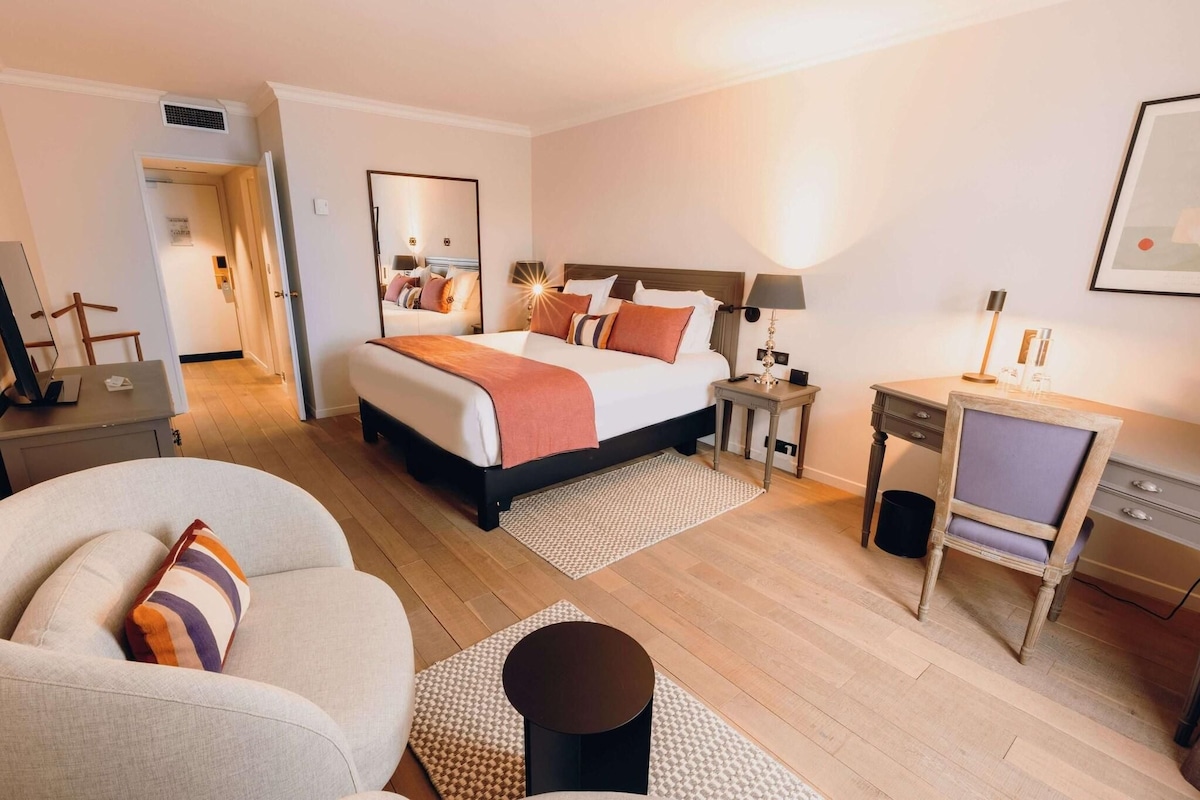 A hotel room with a bed, a desk, a chair, a sofa, and a small table.