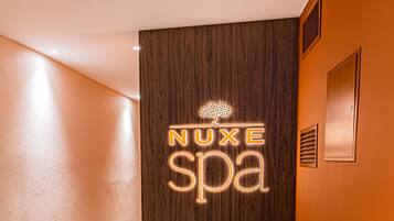 Zona de spa con una silla verde, una mesita con botellas y un letrero de neón que dice "NUXE spa".