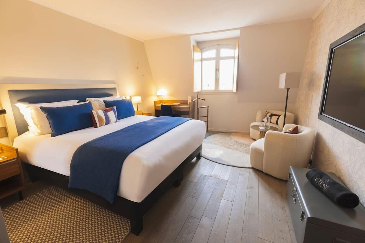 A hotel room with a bed, bedside tables, a desk, a chair, a television, and a window.