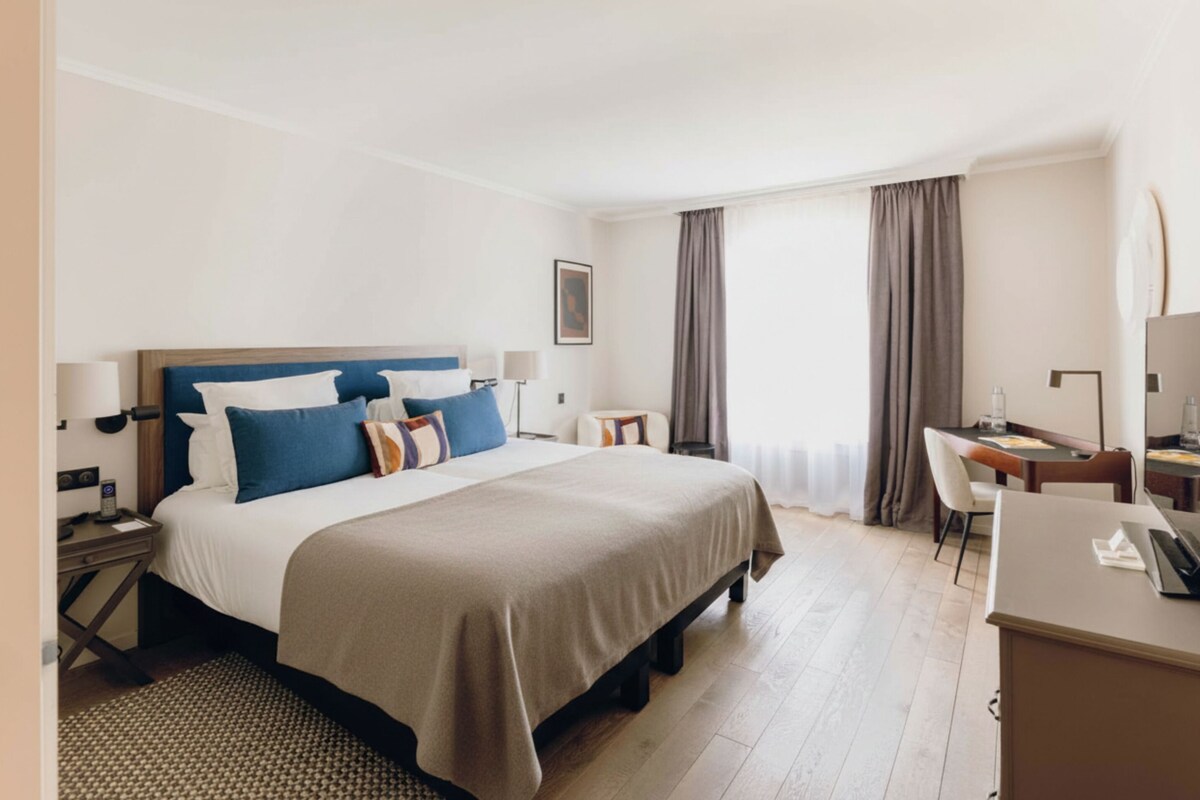 A hotel room with a large bed, a desk, and a chair.