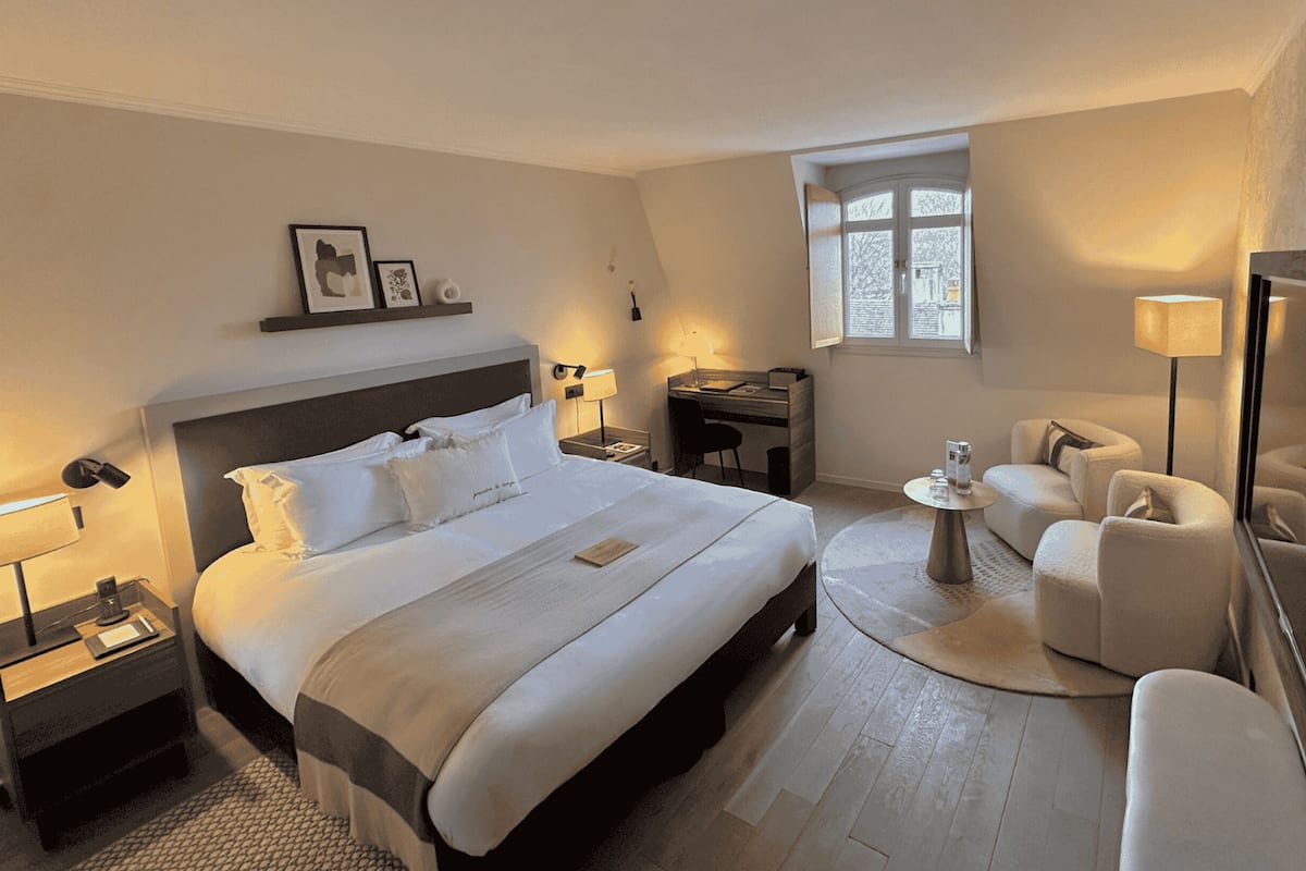 A hotel room with a large bed, a desk, a chair, a small table, and a mirror.
