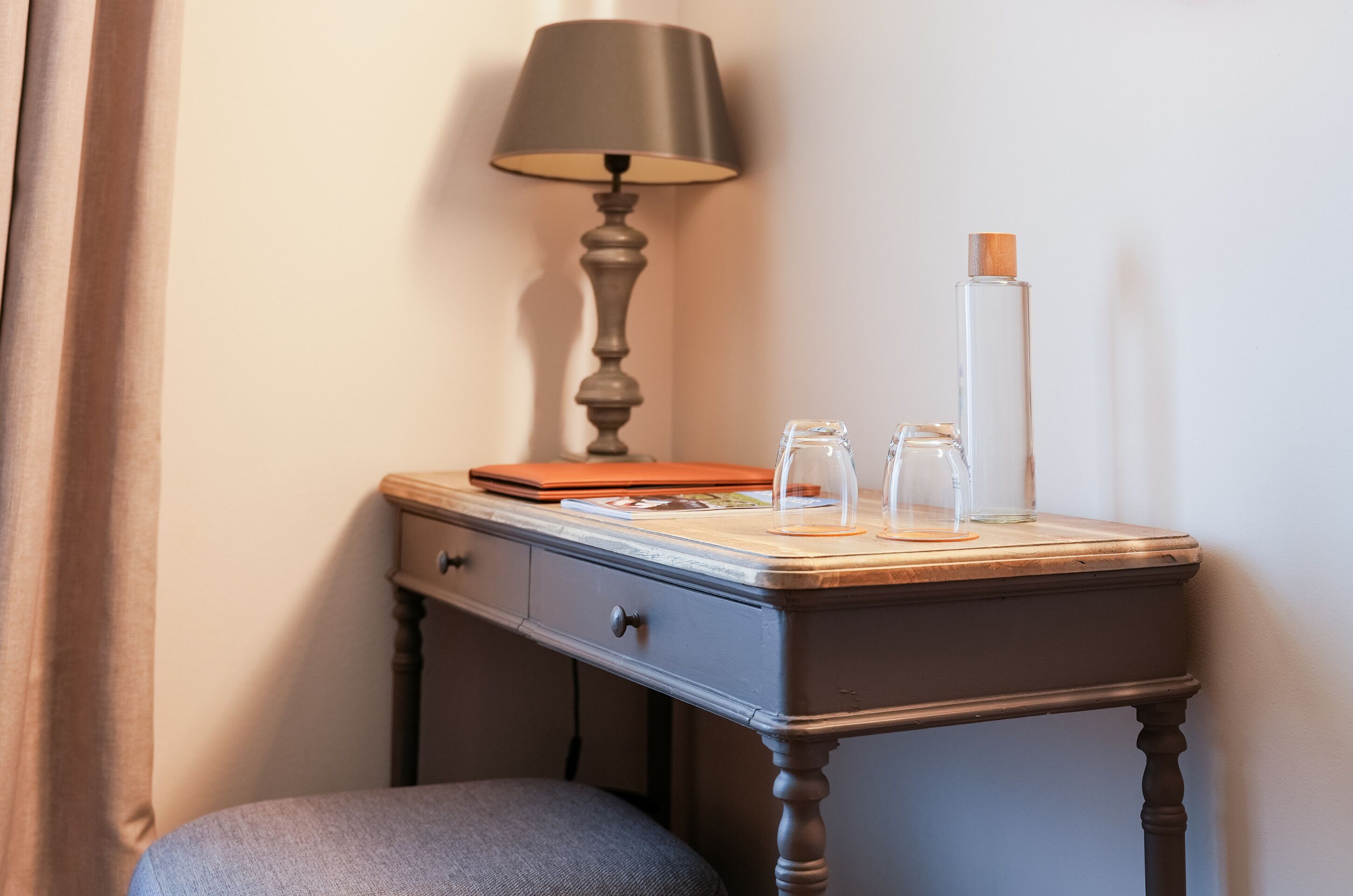 A small wooden desk with a lamp, a glass bottle, and a notebook.