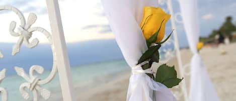 Une structure métallique blanche, ornée d’une rose jaune attachée à celle-ci, surplombe une plage.