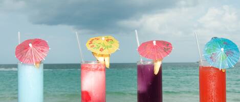 Vier farbenfrohe Cocktails mit Schirmchen auf einer Holztischplatte am Meer.