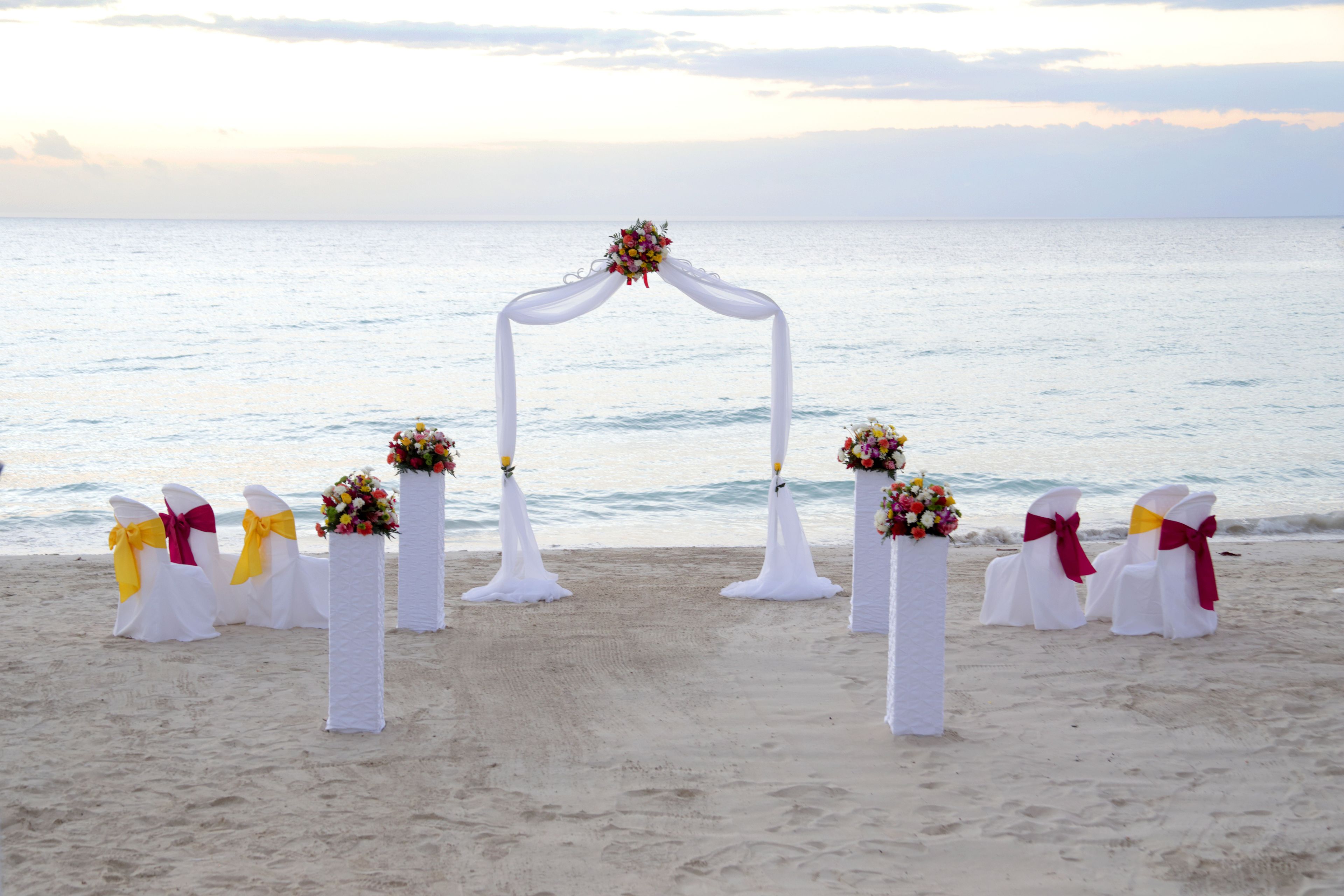 Een buitstoep boog bij een strandbruiloft, met witte stoelen en bloemendecoraties.