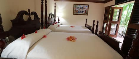 A hotel room with two beds, wooden headboards, a ceiling fan, a painting on the wall, and a window with shutters.