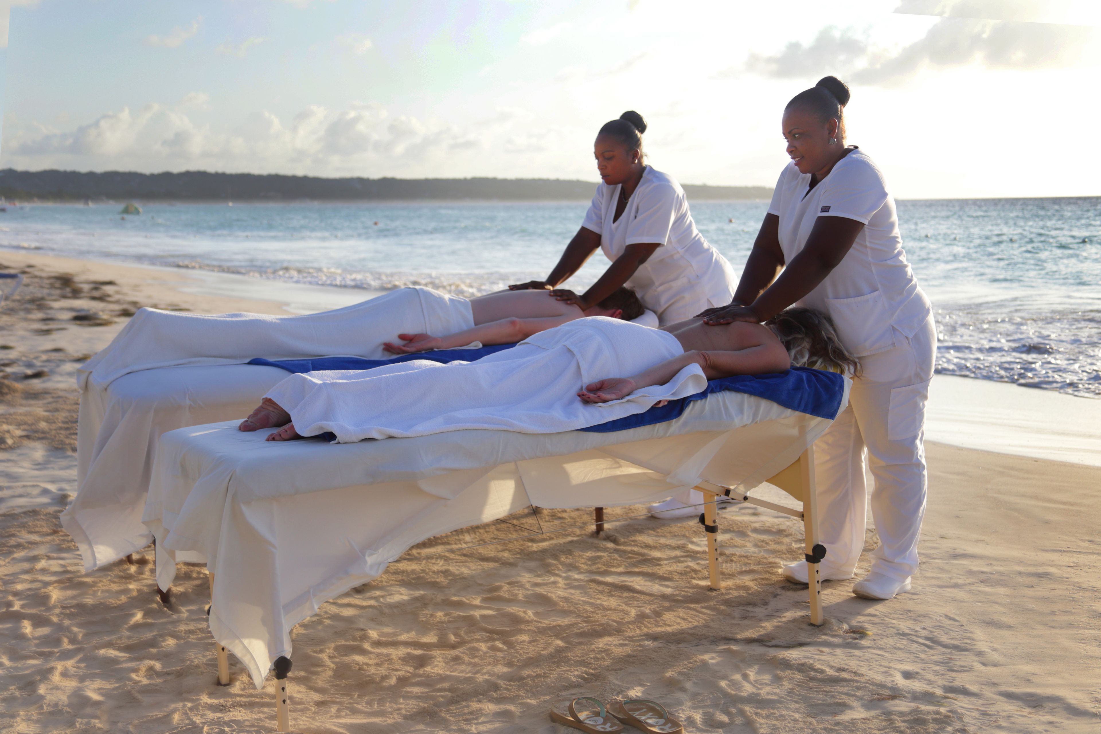 A massage therapy session on a beach with a patient lying on a massage table.