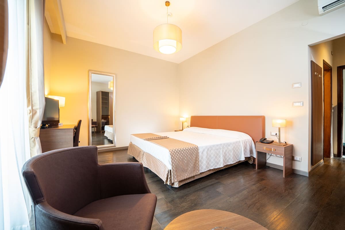 Una habitación de hotel con cama, mesita de noche, lámpara, silla y espejo.