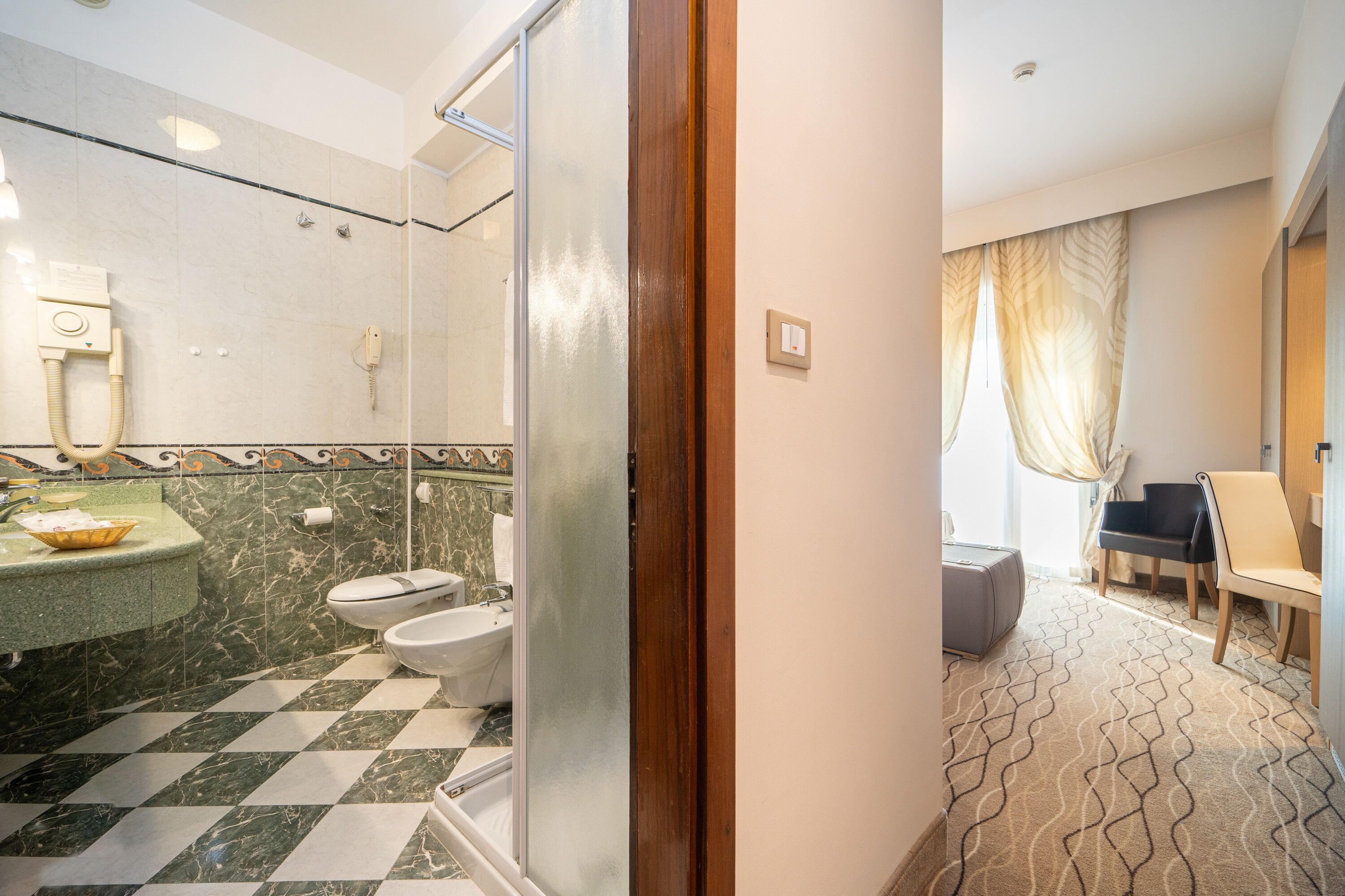 A hotel bathroom with a checkered floor, a glass shower enclosure, a sink with a marble countertop, and a toilet.