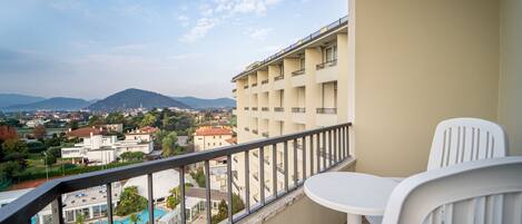 A balcony with a pool view, white chairs, and a building in the background.