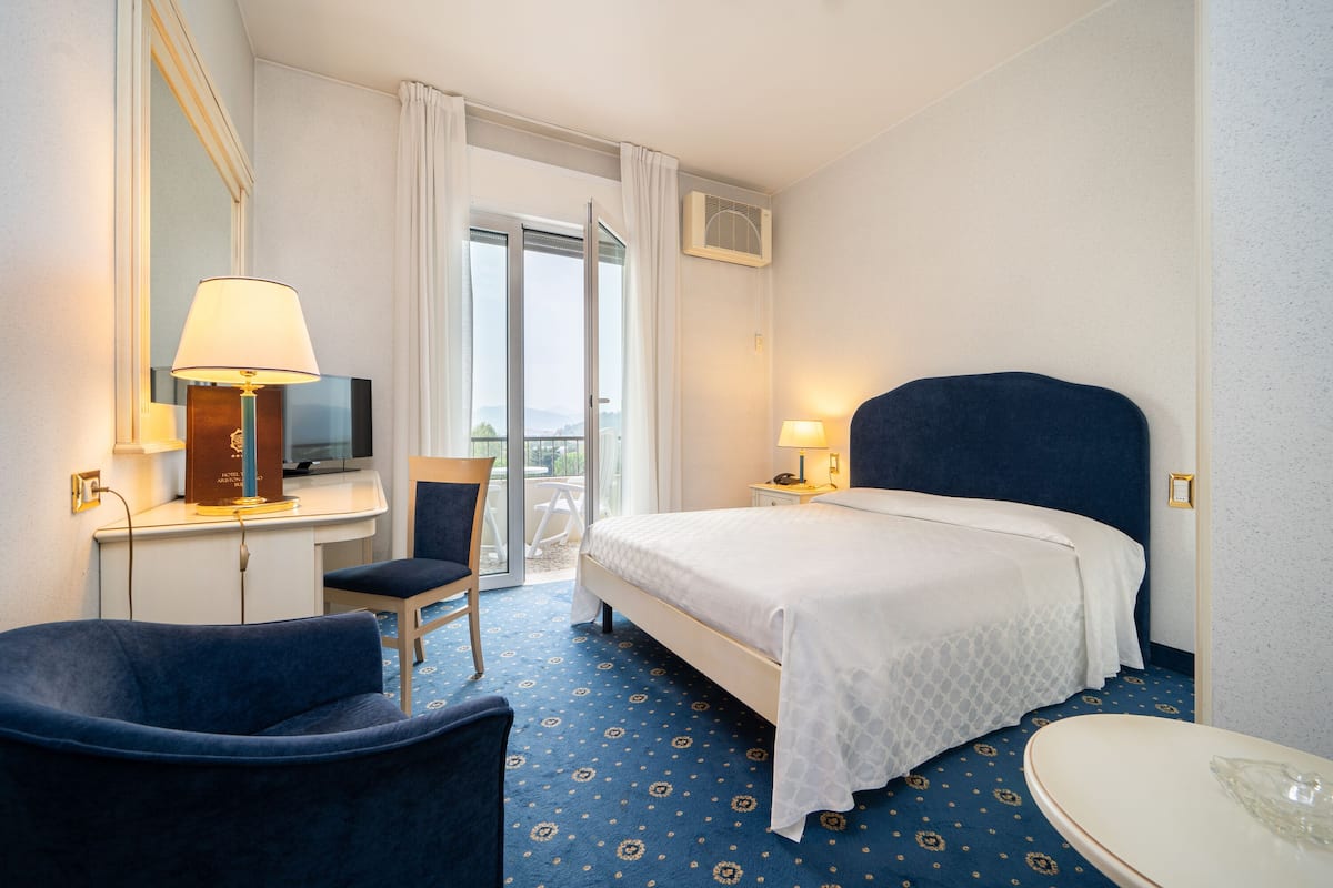 Una habitación de hotel con cama, escritorio con lámpara, una silla, televisor y baño.