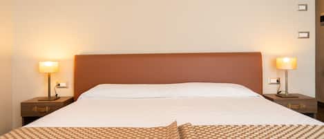 Una cama bien hecha con una colcha estampada, dos mesitas de noche con lámparas y una pared lisa.