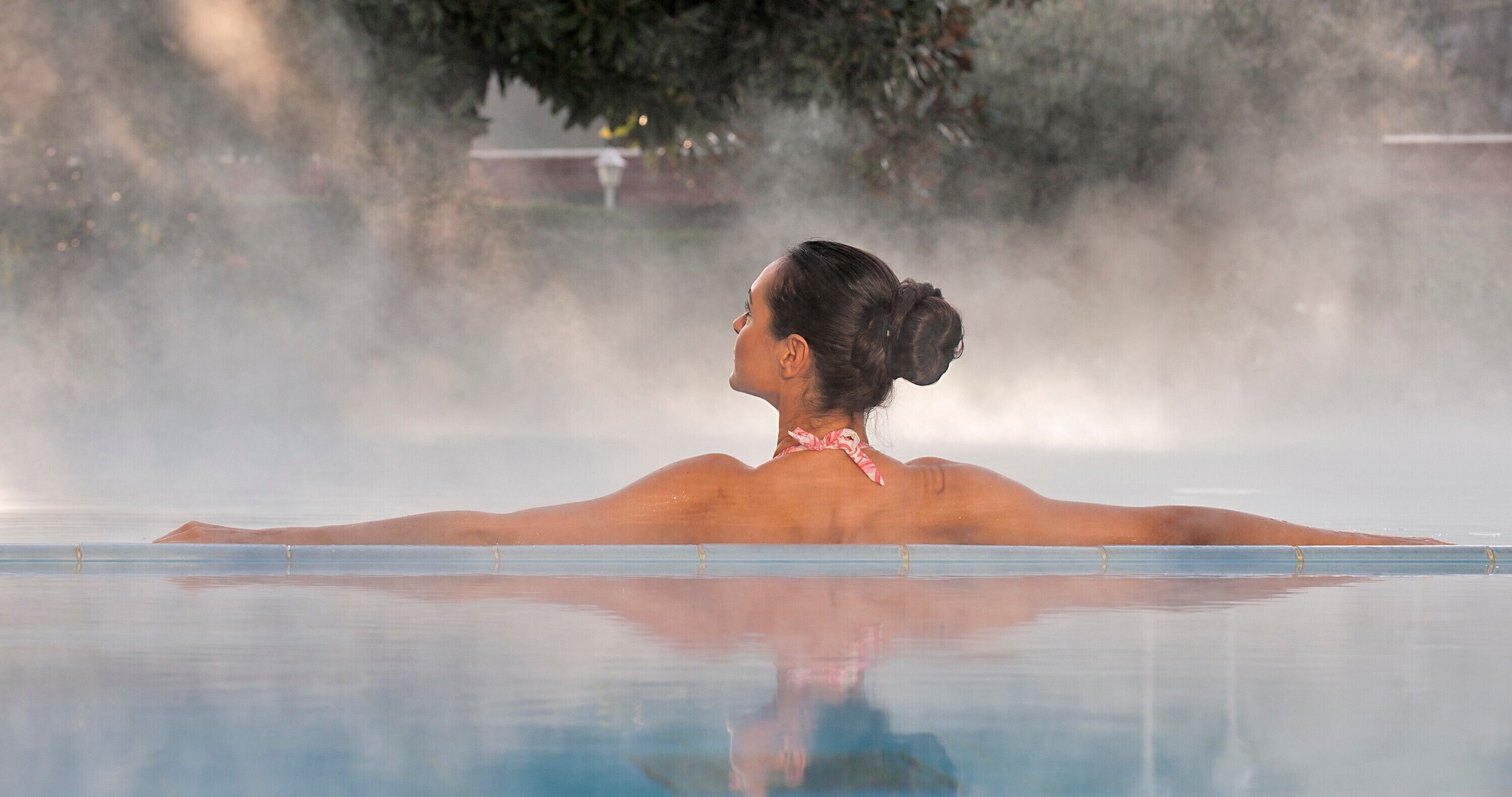 A person in a clear pool with a calm water surface, surrounded by a misty atmosphere.