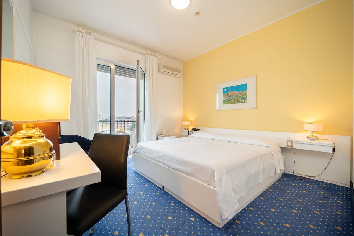 Una habitación de hotel con cama, escritorio, silla y ventana con cortinas.