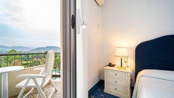 Habitación de hotel con balcón, una cama, una mesita de noche con lámpara y una silla.