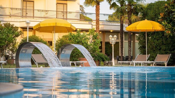 Une piscine agrémentée de deux éléments décoratifs aquatiques, entourée de palmiers et de chaises longues.