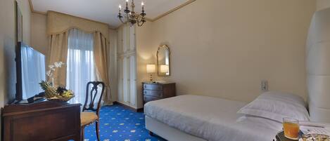 A hotel room with a bed, a desk with a chair, a dresser, a mirror, and a chandelier.
